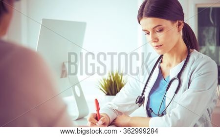 Doctor and patient discussing medical problems in a hospital consulting room. Doc filling in a patient's form