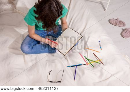 A Girl In A Green T - Shirt And Blue Jeans Is Sitting On The Bed And Writing In A Notebook , Colored