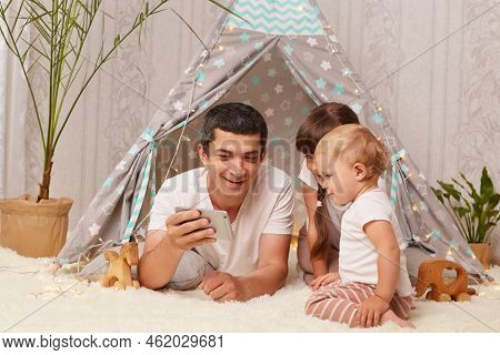 Portrait Of Satisfied Delighted Caucasian Man Wearing White T-shirt With His Children Posing On Floo