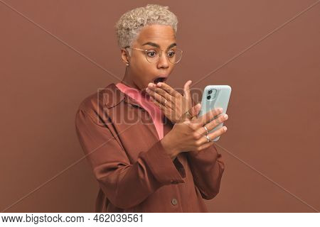 Young Dazed Ethnic African American Woman Holds Phone And Covers Mouth With Hand