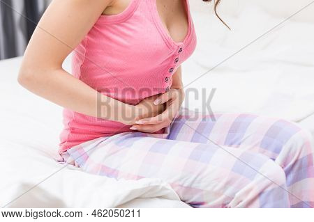 Unhealthy Woman Sitting On Bed Touching Her Stomach Suffering From More Abdominal Pain Or Diarrhea, 