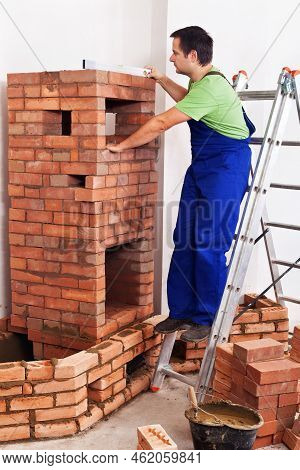 Worker Building Masonry Heater With Bricks And Clay Mortar Laying Around - Checking Level Of The Inn