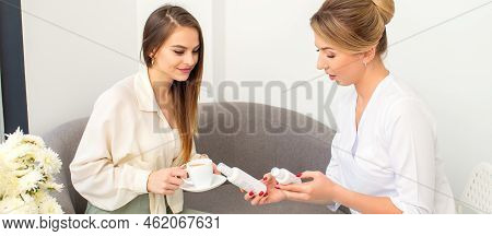 Beautician Offering Product For The Young Woman Holding White Plastic Bottles With A Cream Sitting O
