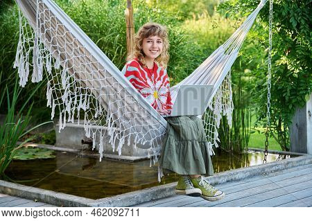 Portrait Of Teenage Girl With Laptop Sitting In Hammock In Backyard