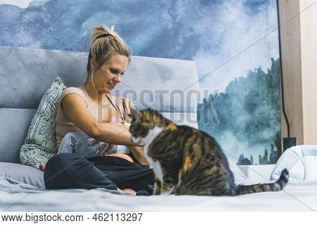 Caucasian Blond Woman Sitting In Bed Holding Infant Boy In Her Arms Brestfeeding With Tricolor Cat S