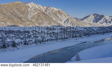 A Blue Ice-free River Flows In A Snow-covered Valley. Thawed Ice Floes Are Visible In The Stream. Re
