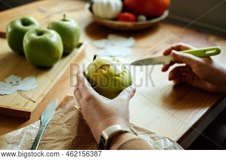 Halloween Diy Fruit Ideas. Female Hands Cutting Out Halloween Green Apple With Creepy Carved Face On