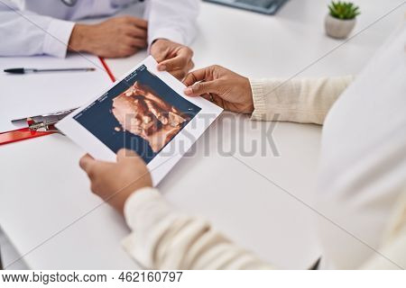 Young latin couple doctor and patient holding baby ecography at clinic
