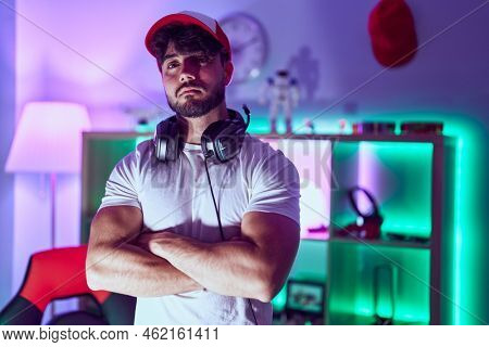 Young hispanic man streamer standing with arms crossed gesture at gamin room