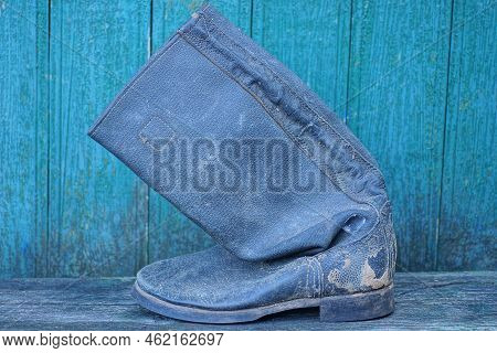One Old Black Dirty Tarpaulin Boot Stands On A Gray Table Against A Green Wall