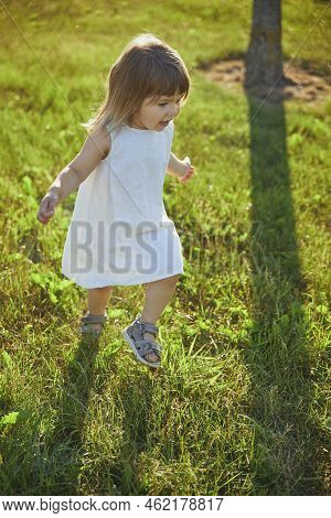 Charming Child In Linen Dress Walking On The Lawn