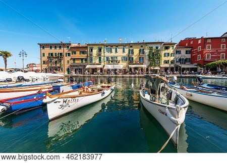 Lazise, Italy - May 26, 2021: Old Port With Small Boats Moored And Colorful Houses Of The Lazise Vil