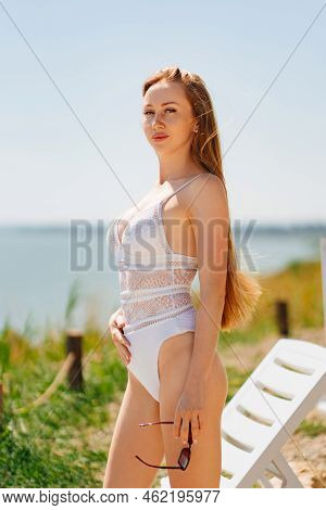 A Long-haired, Slender, Beautiful Woman In A Swimsuit By A Chaise Longue By Sea.