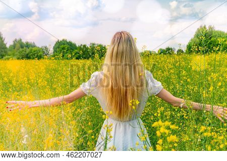 Beautiful Girl In A Flowering Field In A White Dress. Sunbeams, Glare, Light Leaks And Sun Rays. You