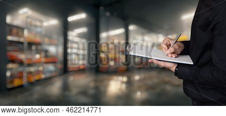 A Man Controls The Goods In A Warehouse To Transfer .a Man Takes Notes On A Blurred Warehouse Backgr