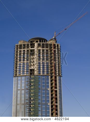 Grúas y construcción de un rascacielos temprano por la mañana contra el cielo azul oscuro