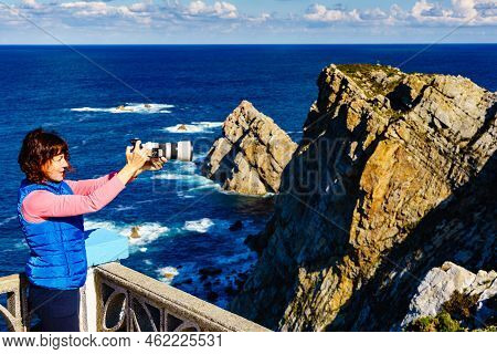 Woman With Camera Take Travel Photo From Seascape Of Atlantic Ocean And Asturias Coast At Cape Penas