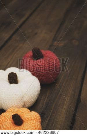 Three Pumpkins Crocheted Stand On A Wooden Table. On A Wooden Table, Knitted Pumpkins Stand In A Row
