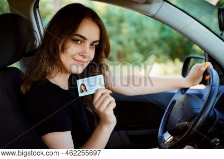 Young Girl With Beautiful Smile Sitting In Car Showing Driving License To The Camera. Woman Has Got 