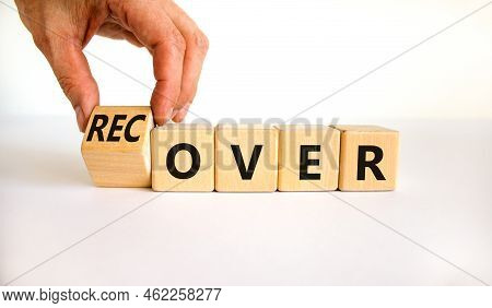 Time To Recover Symbol. Businessman Turns A Wooden Cube And Changes The Word 'over' To 'recover'. Be