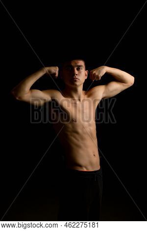 Shirtless 19 Year Old Teenage Boy Flexing His Arms With A Black Background