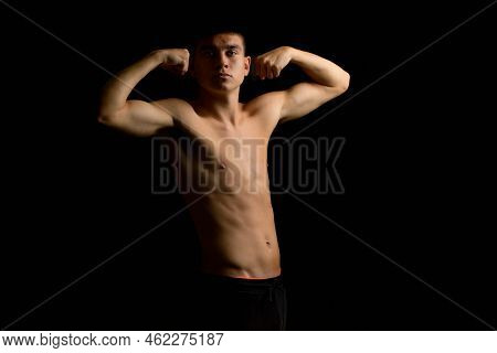 Shirtless 19 Year Old Teenage Boy Flexing His Arms With A Black Background