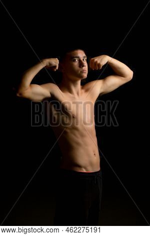 Shirtless 19 Year Old Teenage Boy Flexing His Arms With A Black Background