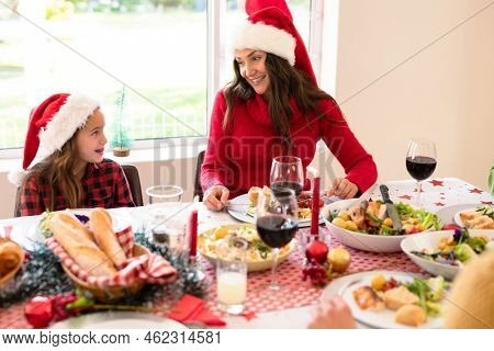 Happymother and daughter wearing santa hats sitting at christmas table. family christmas time and festivity together at home.