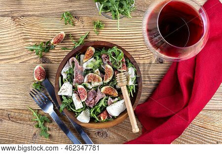 Salad With Arugula , Figs, Prosciutto And Mozzarella And Red Wine On A Wooden Background