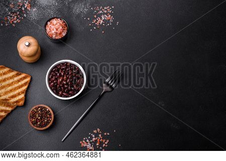 Black, Canned Beans In A White Saucer Against A Dark Concrete Background