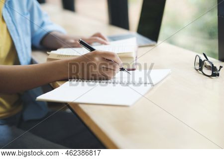 Close Up Of Person Studying, Reading Book, And Taking Notes On Dask Beside The Windows. Woman Taking