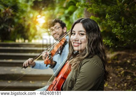 Portrait Of Two Young Violists Sitting Outside. Man And Woman Violinist Sitting On The Stairs. Two Y