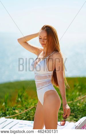 A Long-haired, Slender, Beautiful Woman In A Swimsuit By A Chaise Longue By Sea.