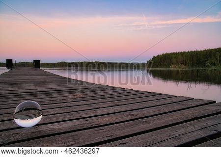 Glass Ball On A Wooden Pier At A Swedish Lake At Evening Hour. Nature Shot From Scandinavia