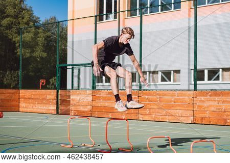 Blond Boy In Sportswear Jumps Over Red Obstacles To Improve Lower Body Dynamics. Plyometric Training