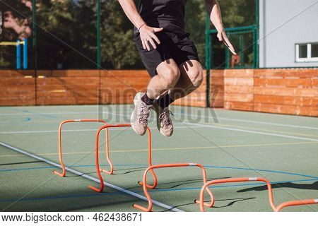 Blond Boy In Sportswear Jumps Over Red Obstacles To Improve Lower Body Dynamics. Plyometric Training