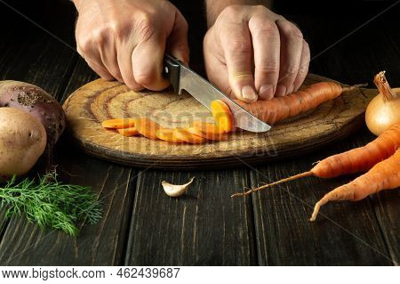 The Cook Cuts Fresh Carot On A Wooden Cutting Board. Close-up Of Chef Hands While Preparing Vegetari