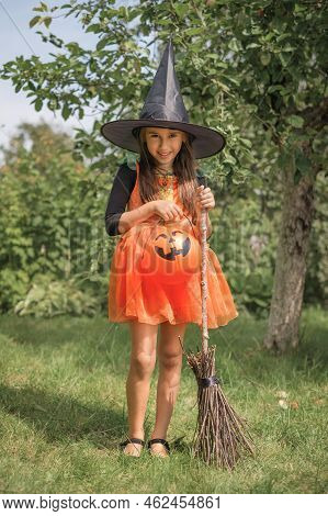 A Small Girl Dressed Up As A Witch With A Bucket In The Shape Of A Pumpkin Goes On A Hunt For Sweets