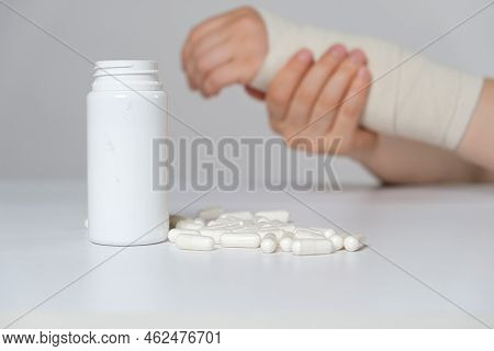 A Persons Hand With An Elastic Bandage And A Jar Of Calcium Or Chondroitin Tablets. Treatment Of Fra
