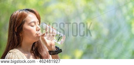 Asian Woman Drinks Water On Green Blur Background