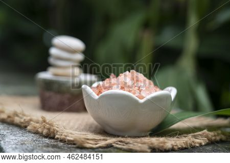 Pink Himalayan Salt In White Ceramic Bowl In Front Of  Meditation Stack Stone  On Green Blurred Back