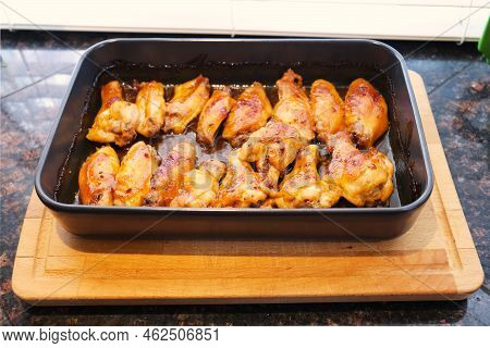 Freshly Baked Chicken Wings In Baking Dish Skillet On Wood Cutting Board On Kitchen Table Counter Su