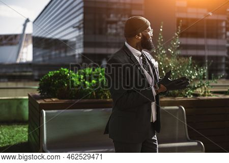 Side View Of A Dapper African Guy With A Nice Beard, In Eyeglasses And A Winter Hat, Tailored Black 