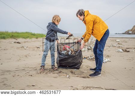 Dad And Son In Gloves Cleaning Up The Beach Pick Up Plastic Bags That Pollute Sea. Natural Education