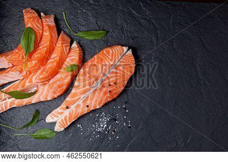 Steak And Slices Of Salmon Filet, Decorated With Spinach Leaves On Black Stone. Top View. Copy Space