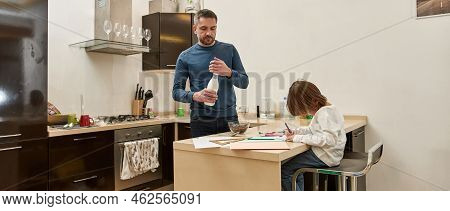 Father Cooking Chocolate Flakes With Milk While Little Son Drawing With Felt-tip Pens At Table At Ho
