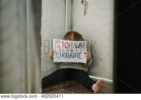 Poor Girl Protesting War Conflict Raises Banner With Inscription Stop War In Ukraine. Kid Sits On Fl