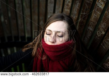 Close-up Portrait Of A Thirty Year Old Attractive White Girl Wearing A Red Winter Scarf, Eyes Closed