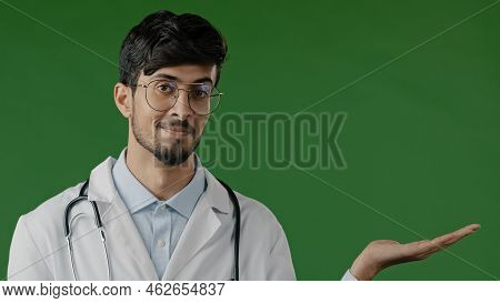 Arab Indian Guy Young Male Doctor Practitioner Man Hold Copy Space On Palm Pointing At Workspace Moc
