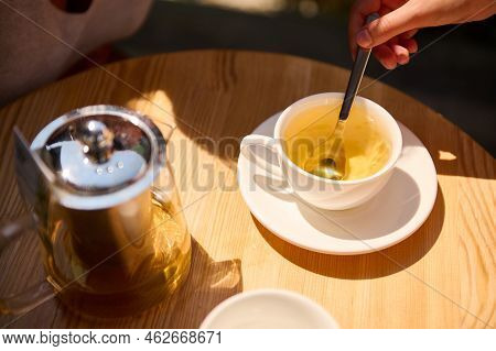 Top View Of A Womans Hand Using A Tea Spoon, Stirring Sugar In The White Teacup With Healthy Antioxi